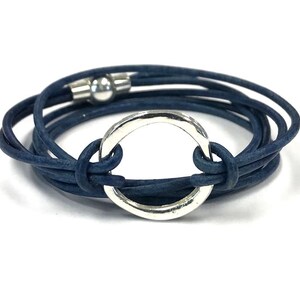 May include: A navy blue leather wrap bracelet with a silver circle charm. The bracelet is made of multiple strands of leather and has a magnetic clasp.