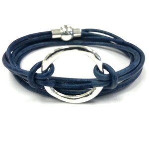 May include: A blue leather wrap bracelet with a silver circle charm. The bracelet is made of multiple strands of leather and has a magnetic clasp.
