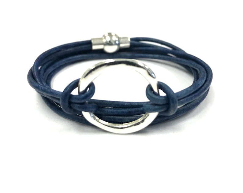 May include: A blue leather wrap bracelet with a silver circle charm. The bracelet is made of multiple strands of leather and has a magnetic clasp.