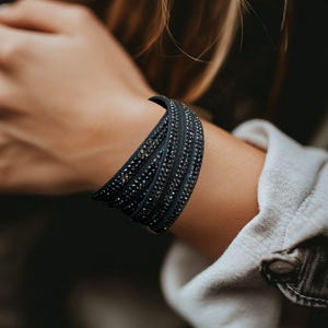 May include: A dark blue wrap bracelet with multiple strands, adorned with small, sparkling embellishments. The bracelet is wrapped around a wrist, showcasing its layered design and textured surface. The jewelry piece adds a touch of elegance.