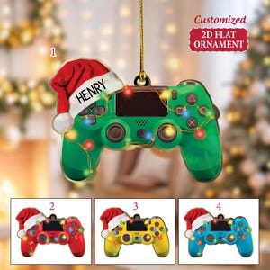 May include: A green video game controller Christmas ornament with a Santa hat that says "HENRY". The ornament is decorated with colorful lights and the text "Customized 2D FLAT ORNAMENT". Additional ornaments are red, yellow, and blue.
