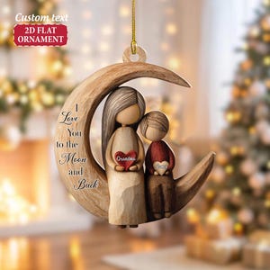 May include: A wooden ornament featuring a mother and child seated on a crescent moon. The mother holds a heart that says "Grandma," and the child holds a heart that says "James." The ornament has the text "I Love You to the Moon and Back."