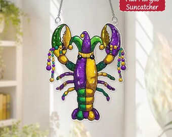 Puede incluir: Un atrapasoles plano de acrílico con forma de langosta, con un esquema de colores de Mardi Gras. La langosta está dividida verticalmente, con un lado morado y el otro dorado. Las pinzas son verdes y moradas, y tiene un gorro de bufón verde y morado. Cuelga de una cadena plateada.