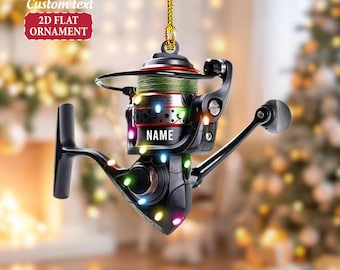 May include: A black and silver fishing reel ornament with green fishing line. The ornament has the word "NAME" on it and is decorated with colorful lights. The text "Custom text 2D FLAT ORNAMENT" is in the upper left corner.
