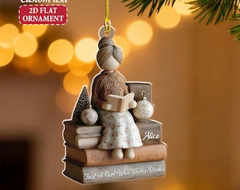 May include: A 2D flat ornament featuring a woman reading a book while seated on a stack of books. The ornament has a brown sweater, floral dress, and a bun hairstyle. The text "Just A Girl Who Loves Books" is visible.