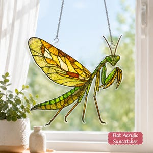 May include: A praying mantis suncatcher featuring stained glass style patterns in shades of green, yellow, and orange. The insect has large wings, thin legs, and antennae, suspended by a silver chain. Text reads: Flat Acrylic Suncatcher.