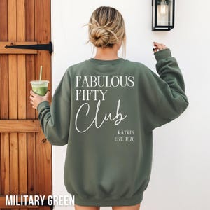 Könnte beinhalten: Militärgrünes Sweatshirt mit dem weißen Text "FABULOUS FIFTY CLUB". Der Name "Katrin" und das Jahr "EST. 1976" sind ebenfalls aufgedruckt. Das Sweatshirt ist einfarbig und hat lange Ärmel.