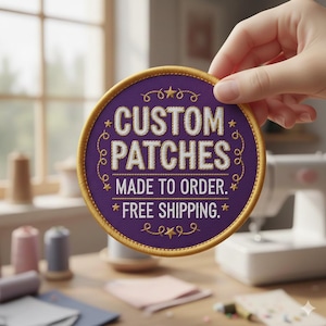 May include: A round, purple patch with gold trim and white text that reads "CUSTOM PATCHES MADE TO ORDER." The patch is held by a hand. The background includes sewing supplies and a sewing machine.