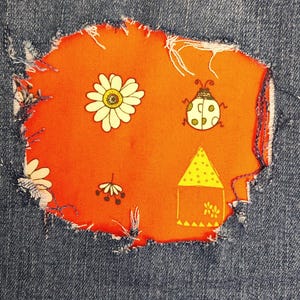 May include: A blue denim fabric featuring a large, frayed-edge orange patch sewn onto the material. The orange patch is decorated with a white daisy, a spotted ladybug, a small floral sprig, and a yellow triangular house with polka dots.