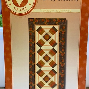 May include: A quilting pattern titled "Turkey Crossing" by Sandy Gervais. The pattern features a brown, orange, and cream quilt design with a floral border.