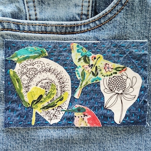 May include: A denim patch with a blue background and colorful embroidered designs. The patch features a butterfly, a flower, and a bird.