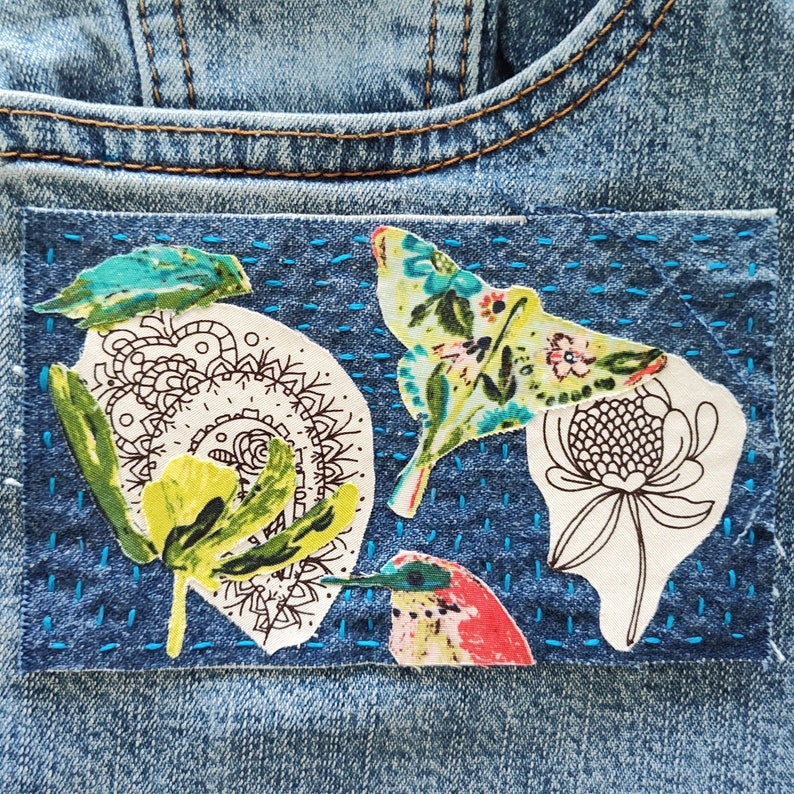 May include: A denim patch with a blue background and colorful embroidered designs. The patch features a butterfly, a flower, and a bird.
