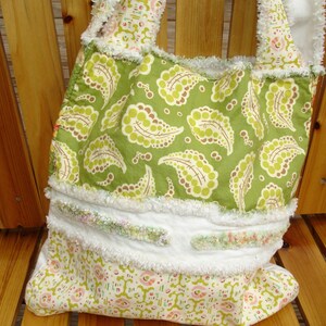 May include: A green and white fabric tote bag with a paisley pattern. The bag has a white crocheted trim and a white fabric lining.