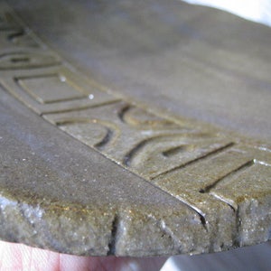 May include: A close-up of a brown ceramic plate with a decorative design around the edge.