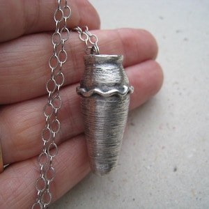 Może przedstawiać: Srebrny naszyjnik z wisiorem w kształcie małego, fakturowanego wazonu. Wazon ma falisty brzeg i fakturowaną powierzchnię.
