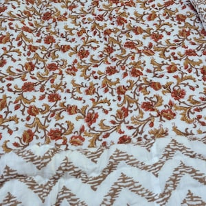 May include: White fabric with a repeating pattern of red and gold floral vines. The bottom portion features a white fabric with a brown zigzag pattern. The fabric is likely used for home decor or textiles.