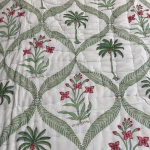 May include: White quilted bedspread featuring a repeating pattern of green palm trees and red flowers. The design is framed by a green leaf pattern. The bedspread has a green border.