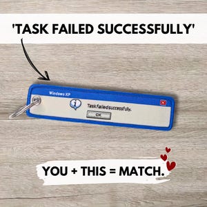 Puede incluir: Un llavero rectangular azul y blanco que presenta un cuadro de mensaje de error al estilo de Windows XP. El gráfico incluye una barra de título azul etiquetada como Windows XP, un icono de información y el texto Task failed successfully.