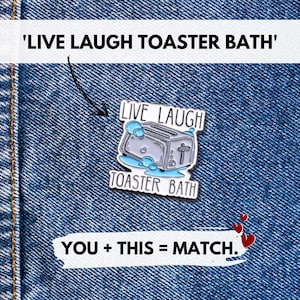 Może przedstawiać: Srebrzysta przypinka emaliowana przedstawiająca toster zanurzony w niebieskiej wodzie z bąbelkami, otoczony napisem 'LIVE LAUGH TOASTER BATH' czarnymi wielkimi literami. Wzór zawiera mały symbol krzyżyka na boku tostera.