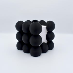 Könnte beinhalten: Schwarzer, würfelförmiger Schreibtisch-Organizer mit einer strukturierten Oberfläche aus runden, schwarzen Kugeln. Der Organizer ist mit weißem Papier gefüllt.