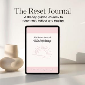 Può includere: Un tablet digitale che mostra "The Reset Journal" con il testo: "A 30 day guided Journey to reconnect, reflect and realign." La copertina del diario presenta un sole. Un vaso beige è a sinistra.