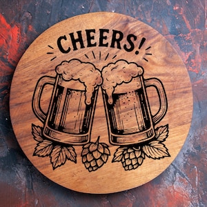 May include: A round wooden coaster with a beer-themed design. The coaster features two beer mugs clinking, with the word "CHEERS!" above them. The design is in black, with hops and leaves at the bottom.