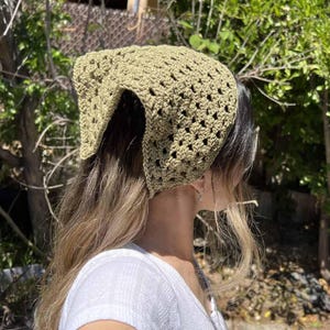 Peut inclure: Un foulard triangulaire vert sauge présentant un motif en crochet ajouré avec un design répétitif en forme de losange. Le foulard est fabriqué en fil et couvre le sommet de la tête, se terminant en pointe à l'arrière du cou.