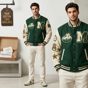 May include: Green and cream varsity jacket with patches, including a mountain scene and the letter "M". The jacket has striped cuffs and a button-up front. The model is wearing cream-colored pants and sneakers. A sign says "YOUR CUSTOM LOGO AVAILABLE".