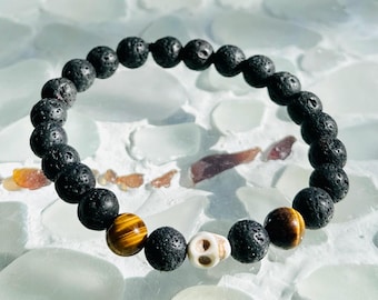 Puede incluir: Un brazalete de piedra de lava negra con cuentas de ojo de tigre y un dije de calavera blanca.