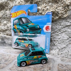 Puede incluir: Un coche de juguete Hot Wheels turquesa con gráficos de "Turbo" y "Honda". El coche se muestra con su embalaje, que incluye el logotipo de Hot Wheels y el texto "NW J-IMPORTS". Es una réplica en miniatura de un vehículo Honda.