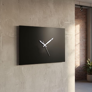 May include: A modern, rectangular black wall clock with silver hands. The clock is mounted on a textured, light gray wall. The hands point to approximately 10:10. The background includes a brick wall, a window, and a potted plant.