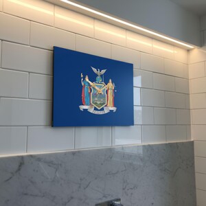 K&ouml;nnte beinhalten: Ein blaues, rechteckiges Wandkunstwerk mit dem Wappen des Staates New York. Das Kunstwerk ist an einer wei&szlig; gefliesten Wand &uuml;ber einer Marmorarbeitsplatte angebracht. Das Wappen zeigt Figuren, einen Adler und das Wort "Excelsior".
