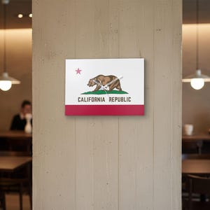 K&ouml;nnte beinhalten: Eine quadratische Wanduhr mit dem Design der kalifornischen Staatsflagge. Das Zifferblatt zeigt das B&auml;renemblem des Staates, einen roten Stern und die Worte "CALIFORNIA REPUBLIC". Der untere Teil ist rot, mit wei&szlig;em Hintergrund.