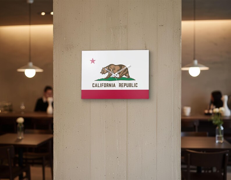 K&ouml;nnte beinhalten: Eine quadratische Wanduhr mit dem Design der kalifornischen Staatsflagge. Das Zifferblatt zeigt das B&auml;renemblem des Staates, einen roten Stern und die Worte "CALIFORNIA REPUBLIC". Der untere Teil ist rot, mit wei&szlig;em Hintergrund.