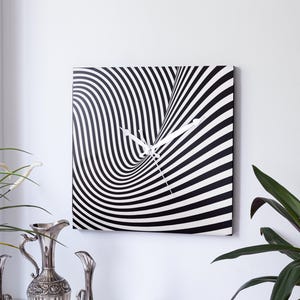 May include: Square wall clock with a black and white striped design creating an optical illusion. The clock hands are white. The clock is mounted on a white wall. The overall theme is home decor.