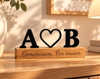 May include: A decorative wooden block featuring the black letters A and B separated by a black heart outline. The light-colored wooden base is engraved with the German text "Gemeinsam. Für immer." in a cursive script font on the front face.