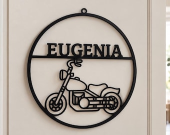 May include: A circular black metal wall sign featuring a cutout design of a motorcycle positioned below the name EUGENIA in bold capital letters. The sign has a small circular loop at the top for hanging and is mounted on a light-colored door.