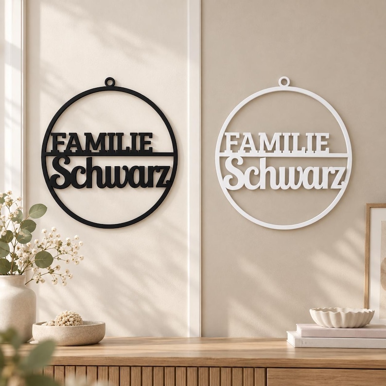 May include: Two circular wall signs, one black and one white, each featuring a horizontal bar dividing the circle. The text FAMILIE is printed in a bold, sans-serif font above the bar, and Schwarz is in a cursive script font below the bar.