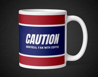 May include: White ceramic coffee mug with red, white and blue stripes. The mug has the text "CAUTION" in bold white letters and the text "MONTREAL FAN WITH COFFEE" in smaller white letters.