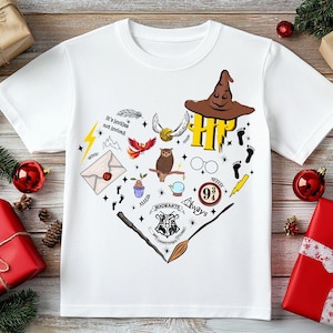 May include: White t-shirt with a heart-shaped design featuring Harry Potter illustrations. Includes a sorting hat, owl, lightning bolt, and the Hogwarts crest. The shirt is surrounded by Christmas decorations.