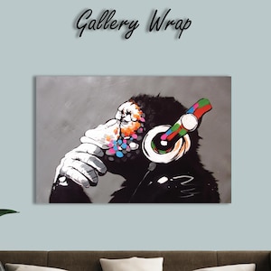 May include: A framed canvas print featuring a monkey wearing headphones. The monkey's face is partially obscured, with colorful paint splatters on its head and hand. The headphones have a vibrant, multicolored design. The words "Gallery Wrap" are above the print.