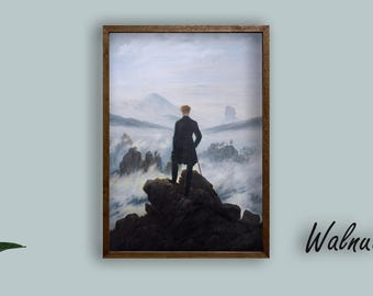 May include: A framed print of a man standing on a rocky peak, overlooking a misty landscape. The artwork is in a walnut frame, with the text "Walnut Frame" in the lower right corner. The print hangs above a brown sofa with white pillows.