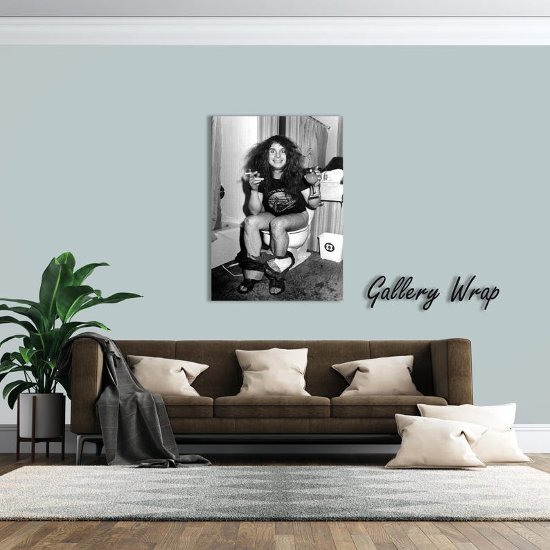 May include: A black and white gallery wrap canvas print featuring a person with long hair sitting on a toilet, holding a cigarette and a glass. The person wears a dark t-shirt and shorts, with a small waste bin visible nearby in the bathroom setting.