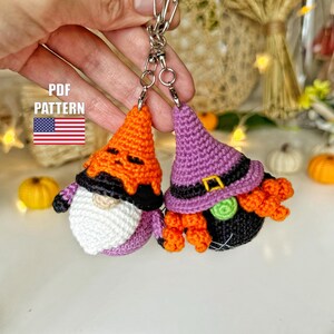 May include: Two crocheted Halloween-themed keychains. One is a gnome with an orange hat and a white beard. The other is a witch with a purple hat and orange hair. Both have black eyes and a black mouth.
