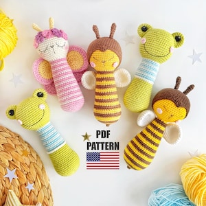 May include: A selection of handmade crochet baby rattles shaped like a butterfly, bees, and frogs. The rattles are in shades of pink, yellow, brown, and green. The image also features the text "PDF PATTERN" and the American flag.