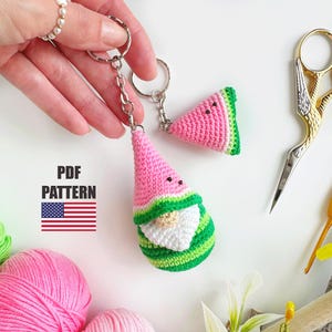 Puede incluir: Llaveros de ganchillo con temática de sandía. Un llavero presenta un gnomo con un sombrero rosa y un cuerpo a rayas verdes, el otro una rodaja de sandía. Los llaveros están unidos a llaveros plateados. La imagen incluye el texto "PDF PATTERN" y la bandera estadounidense.