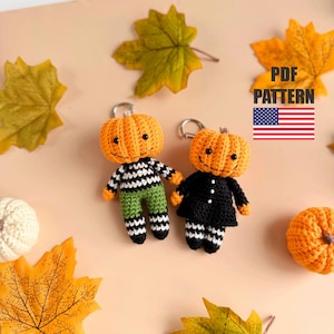 Puede incluir: Dos llaveros de calabaza de ganchillo hechos a mano con caras sonrientes. Una calabaza lleva una camisa a rayas blancas y negras y pantalones verdes, la otra lleva un vestido negro. Los llaveros son de color naranja y negro. La imagen incluye hojas de otoño y el texto "PDF PATTERN".
