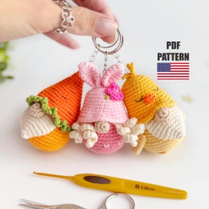 Könnte beinhalten: Gehäkelte Schlüsselanhänger mit Karotten-, Hasen- und Küken-Zwerg-Design. Die Karotte ist orange, der Hase rosa mit einer Blume und das Küken gelb. Die Schlüsselanhänger sind an einem silbernen Ring befestigt. Der Text "PDF PATTERN" ist ebenfalls enthalten.