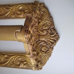 May include: An ornate gold curtain rod with detailed floral and scrollwork carvings. The rod has a decorative centre piece and frame, adding elegance to any window treatment. The design is reminiscent of classic, vintage styles.