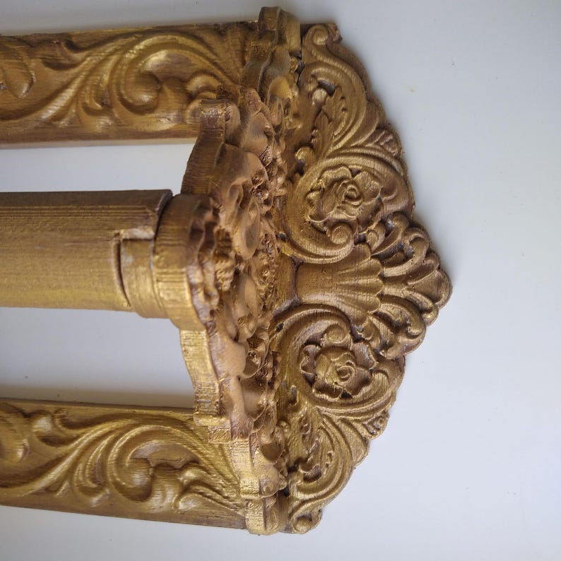 May include: An ornate gold curtain rod with detailed floral and scrollwork carvings. The rod has a decorative centre piece and frame, adding elegance to any window treatment. The design is reminiscent of classic, vintage styles.